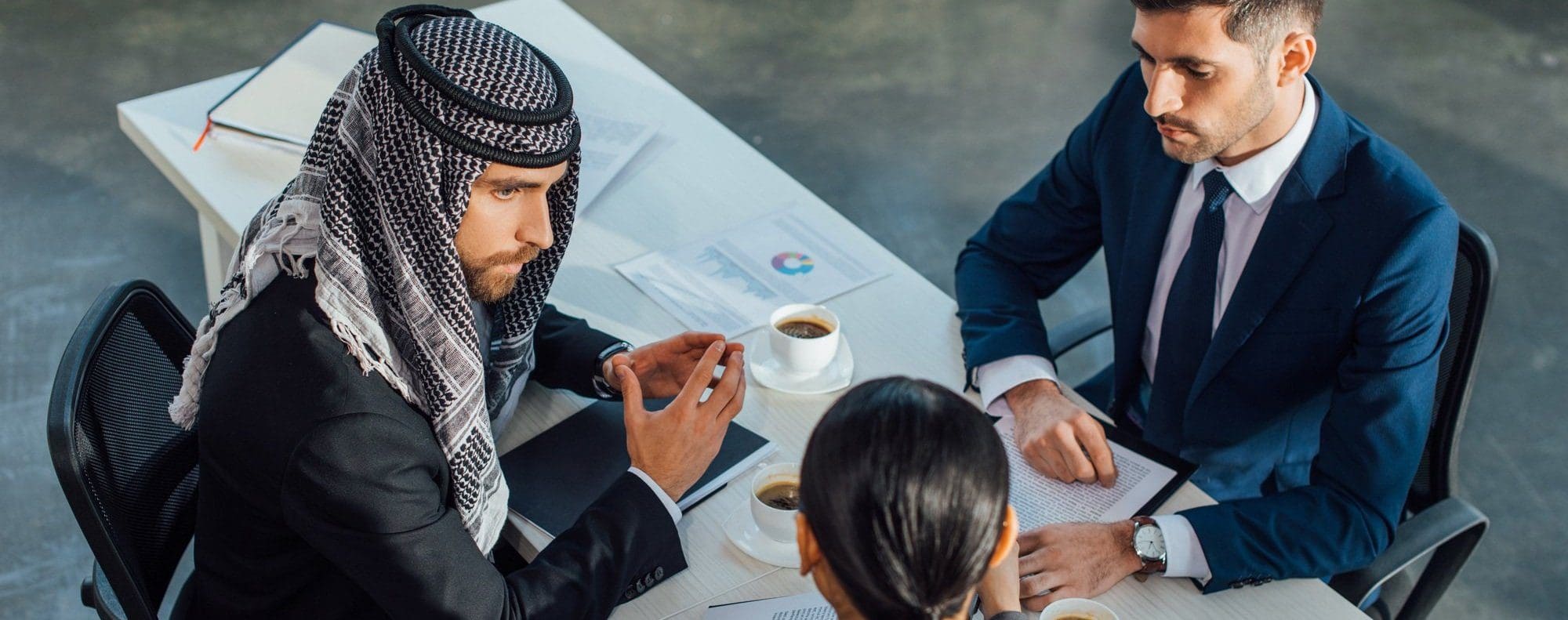 2 business man and one female interpreter sat at a desk, the interpreter is talking to one of the men.