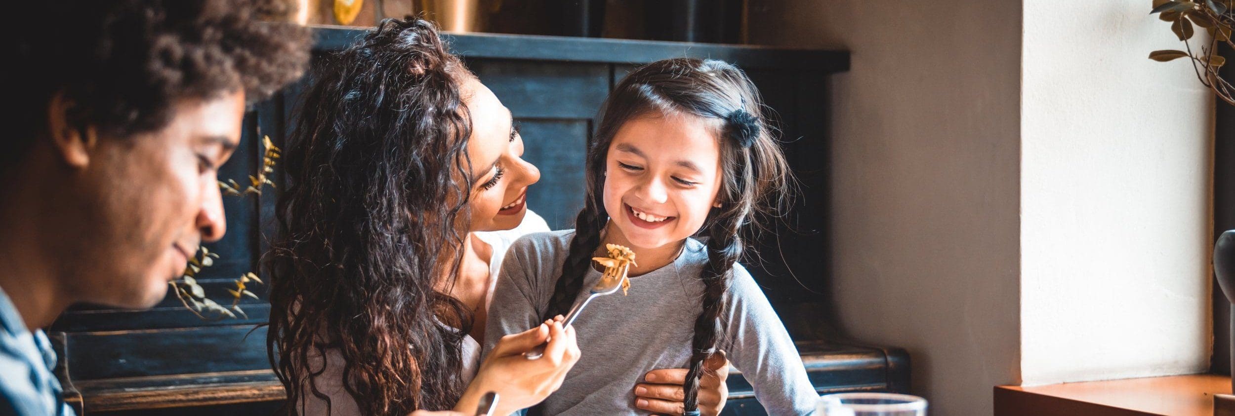 a family eating a meal together, the mother is feeding her daughter