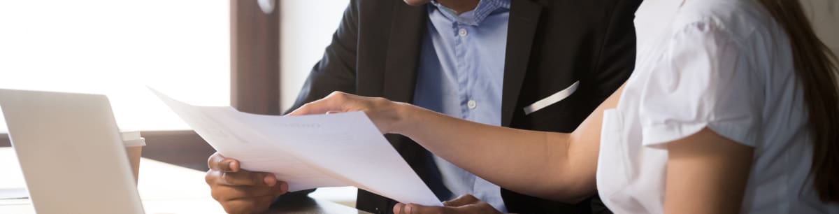 Two people sitting next to each other at a desk, looking at a document together.