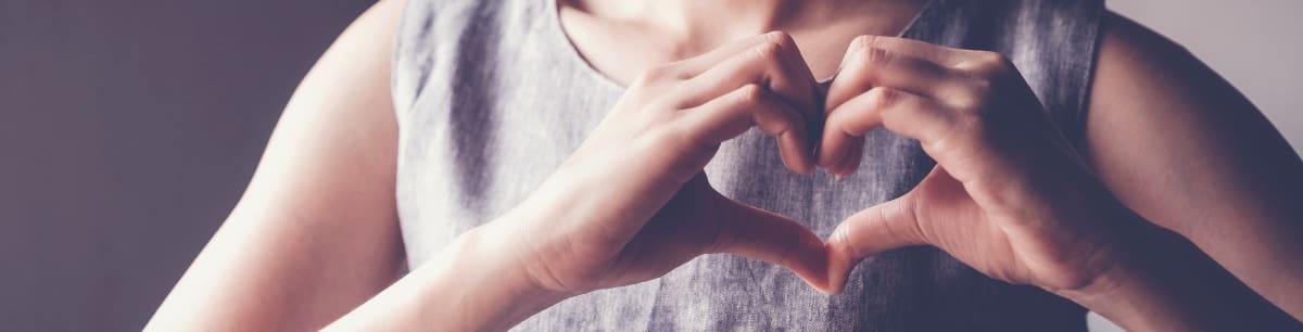 A woman forming a heart shape with her hands held in front of her chest.