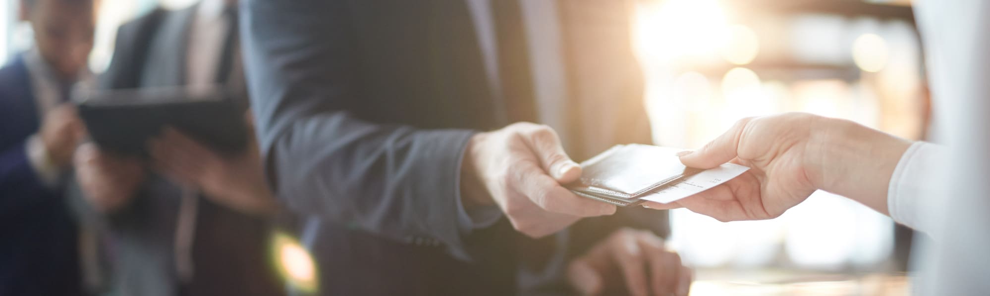 Man in a suit and tie hands over his passport while checking in at an airport.