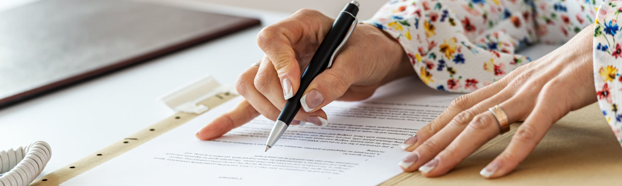 Close-up of a woman's hands holding a pen while reviewing a document.