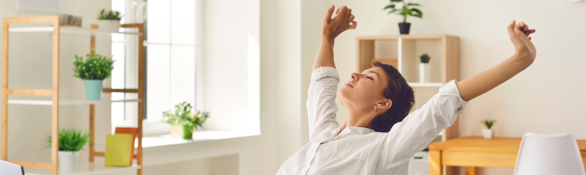 Woman relaxing with arms stretched above her head, leaning back on her chair with eyes closed.