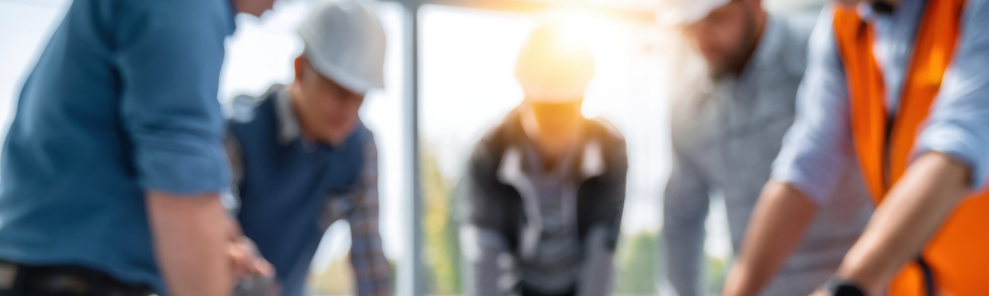 A group of construction workers standing round a table all looking at plan documents, blurred.