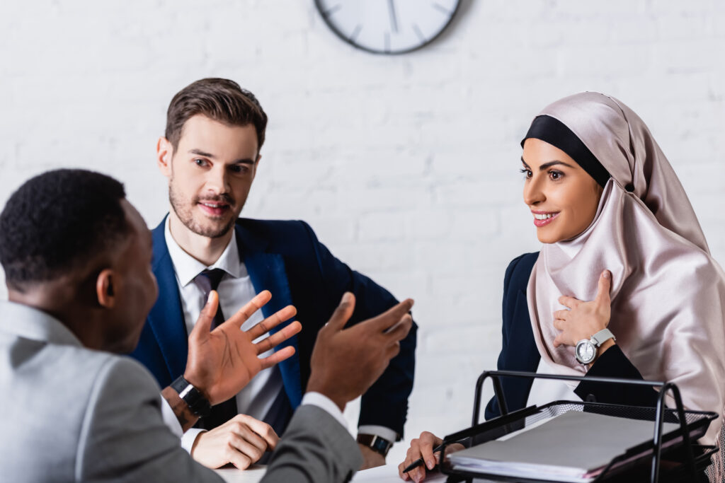 Three people sit at a table discussing work, with hands visible gesturing during conversation.