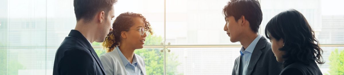 4 business people stood up near a window, one person is translating for the group.