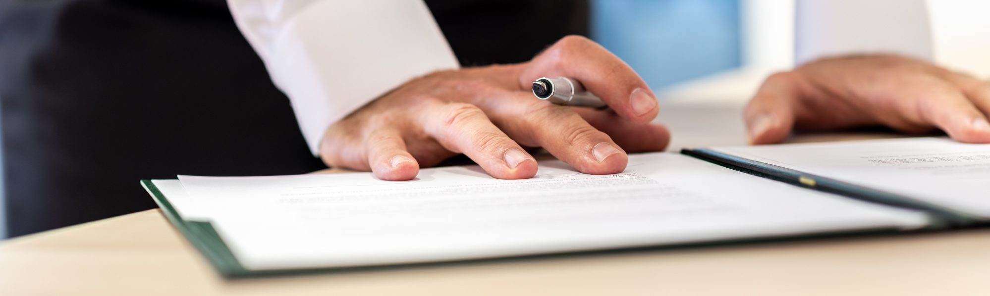 Close‑up of a hand holding a pen while reviewing and signing documents on a desk.