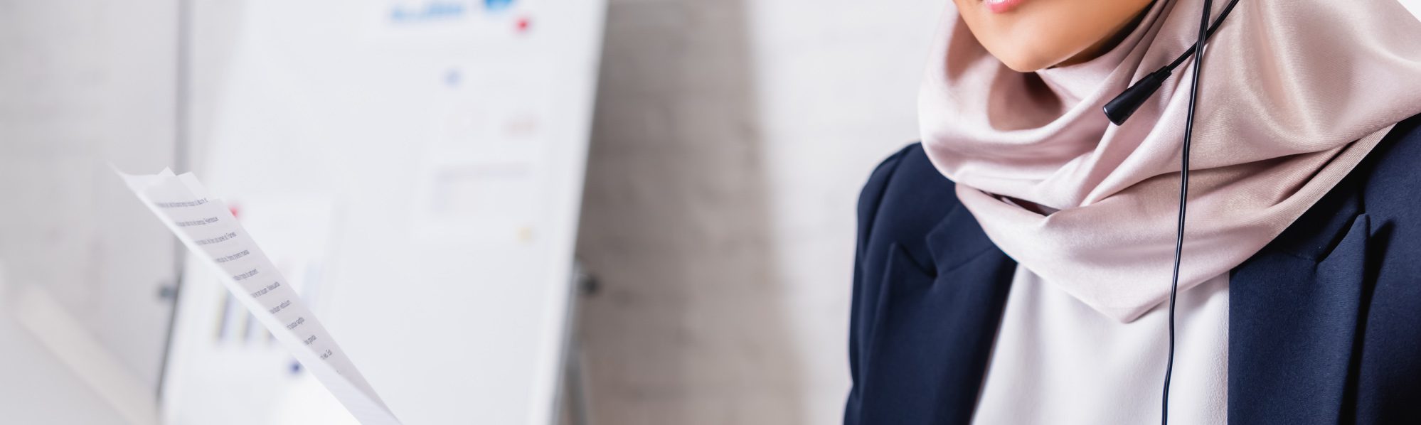 Person using a laptop and headset while reviewing printed documents at a desk.