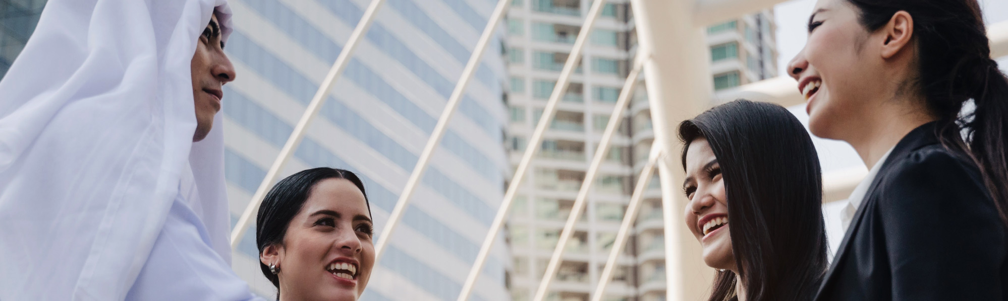 Group of professionals talking together outdoors in a modern urban setting with glass buildings behind.
