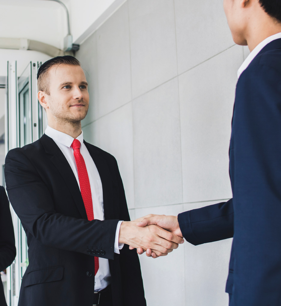 Two people in suits shaking hands in an office setting during a professional meeting.