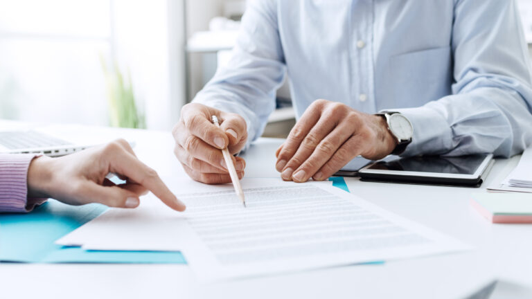 Close-up of two people reviewing a document, one pointing while another holds a pen.