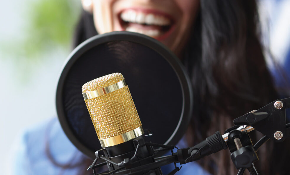 Close-up of a microphone with a person speaking behind it in a recording setup.