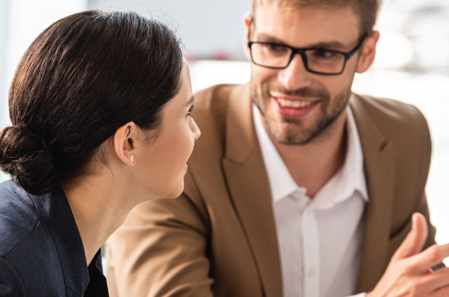 Two people in business attire speak and look at each other during a meeting indoors. Provide your feedback on BizChat