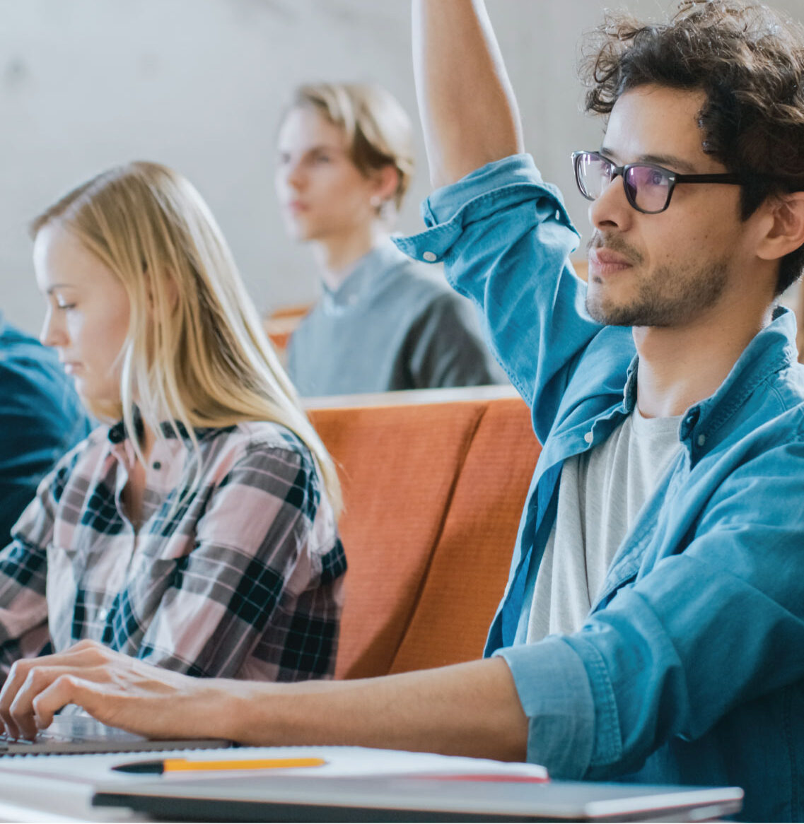 Person raising a hand while seated at a desk with others in a classroom.