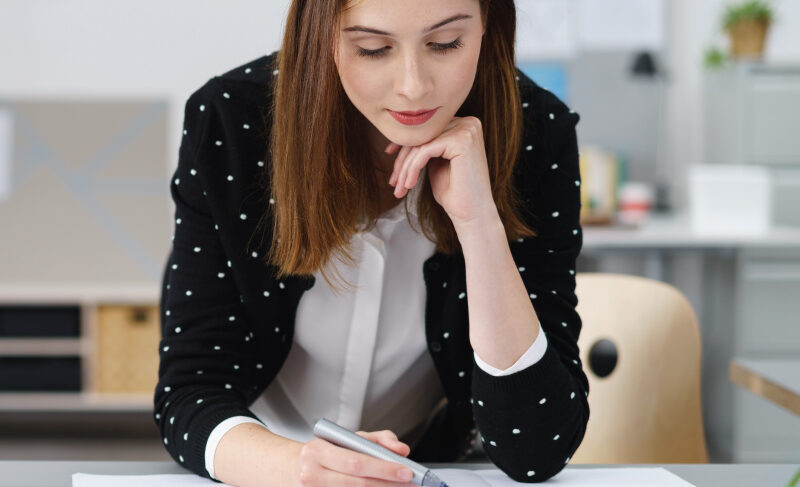 Close-up of a person holding a pen and writing on papers at a desk.