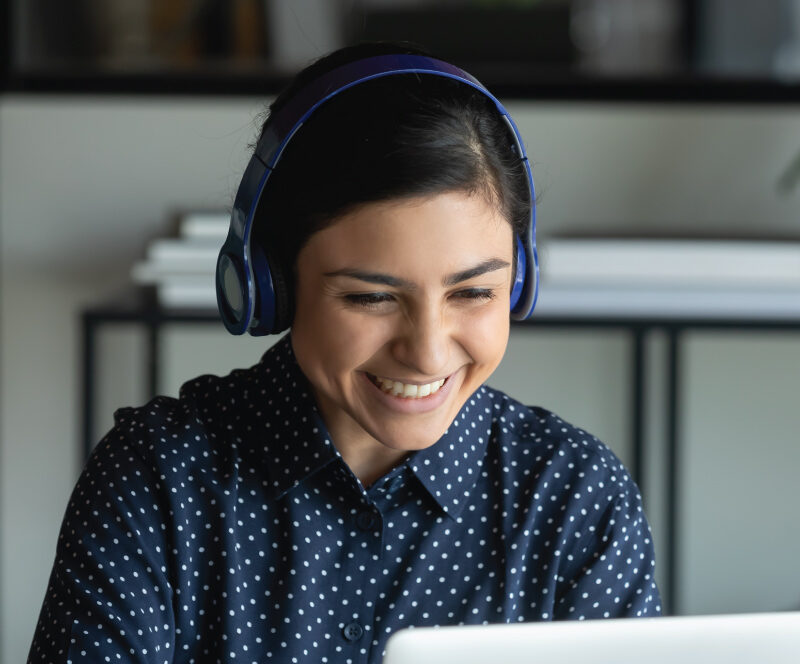 Person wearing headphones uses a laptop while seated at a desk indoors.