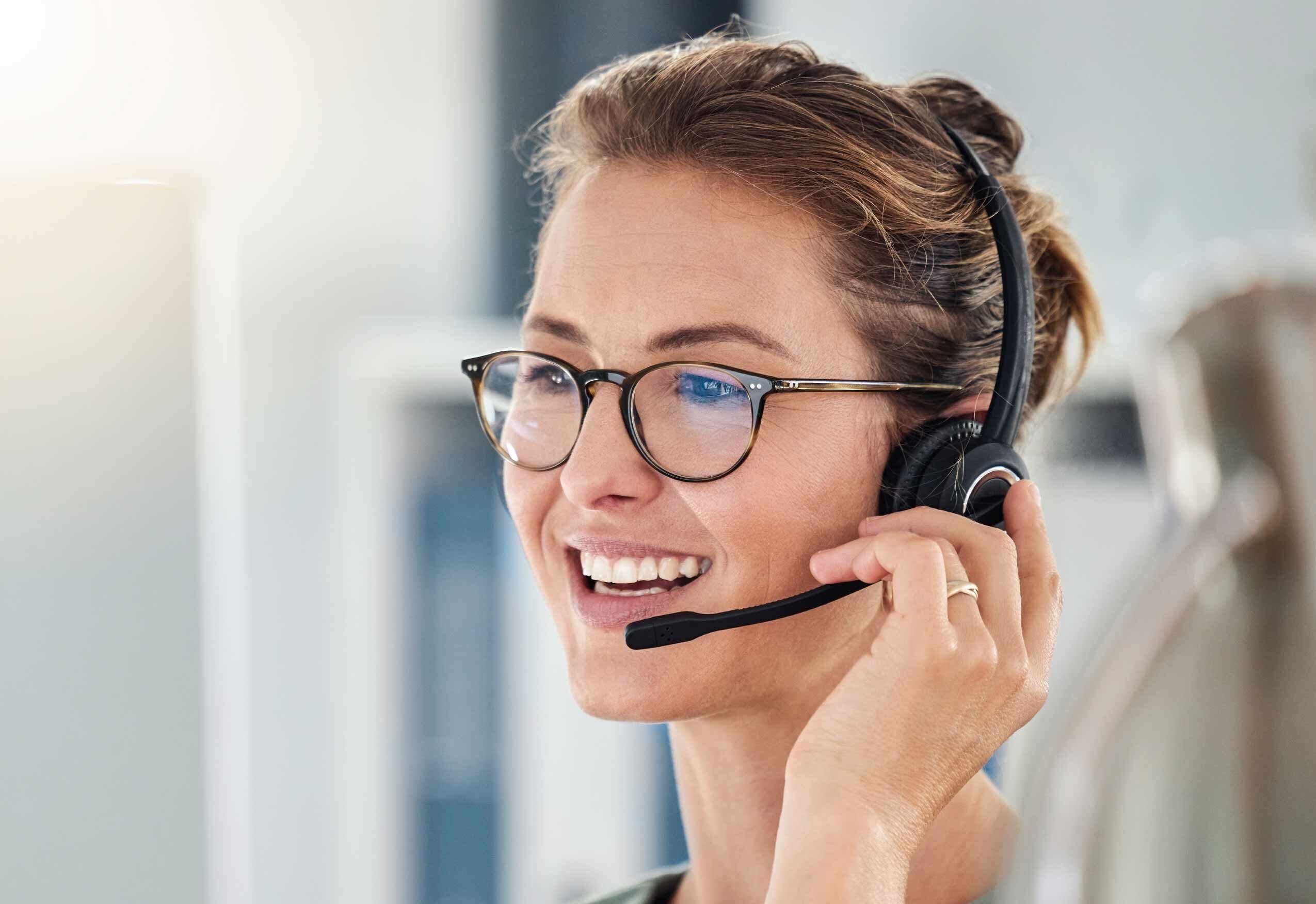 Close‑up of a person wearing a headset speaking on a call in an office setting.