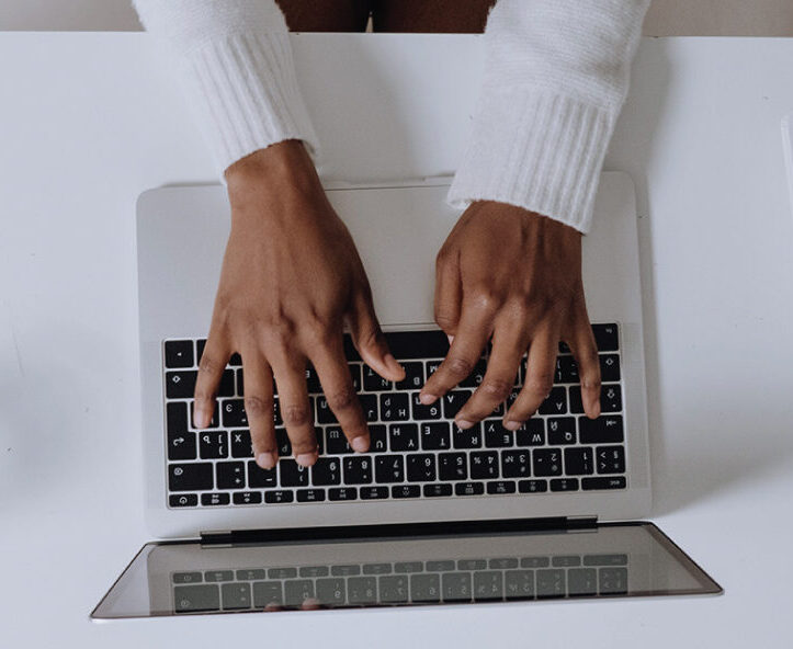 Overhead view of hands typing on a laptop beside a notebook and water glass.