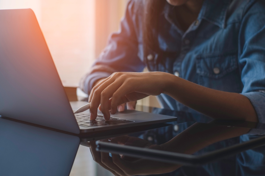 Close-up of hands typing on a laptop with a tablet and stylus on a desk. Provide your feedback on BizChat