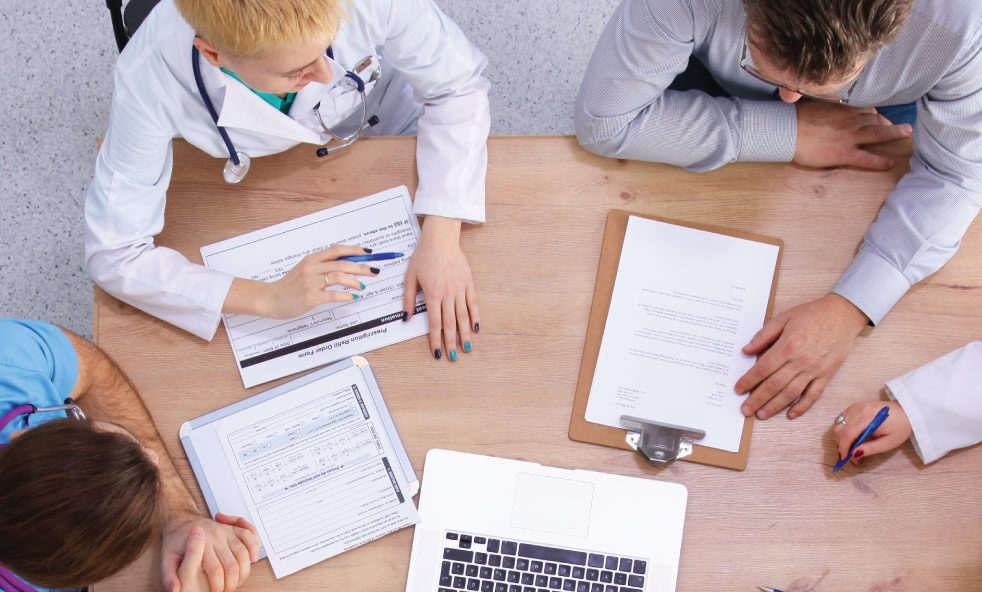 Overhead view of four people reviewing paperwork, forms and a laptop at a table.