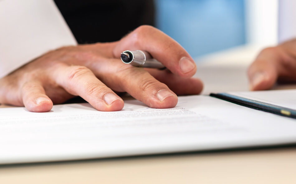 Close-up of a hand holding a pen while signing a document on a desk.