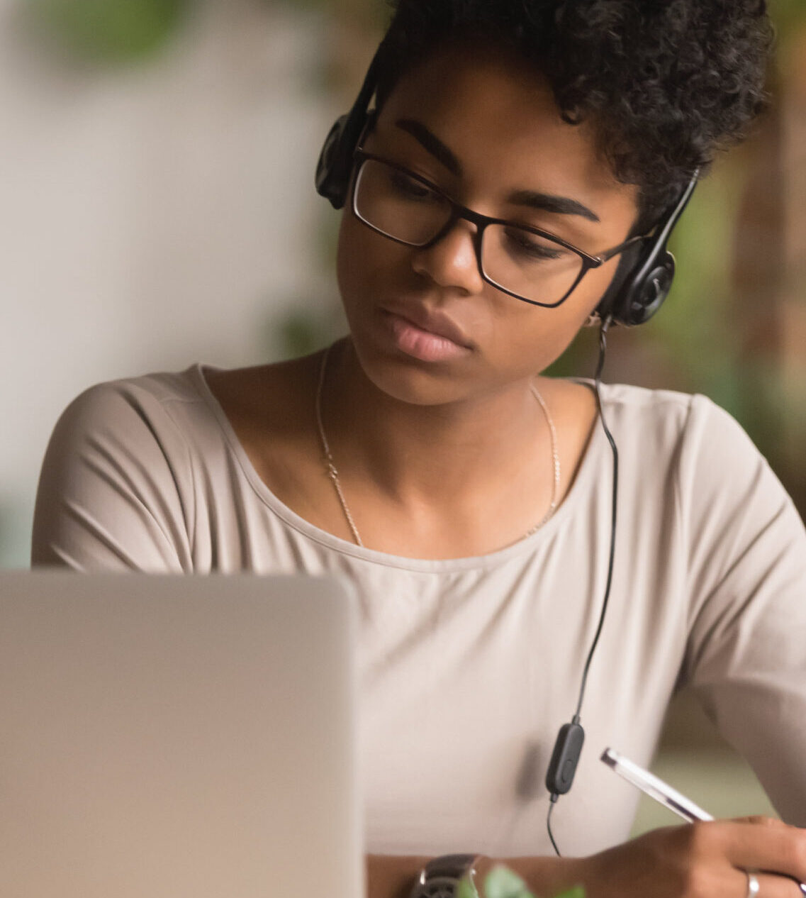 Close-up of a person wearing headphones, writing while using a laptop at a desk.