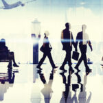 Silhouettes of people walking through an airport with reflections and a plane outside.