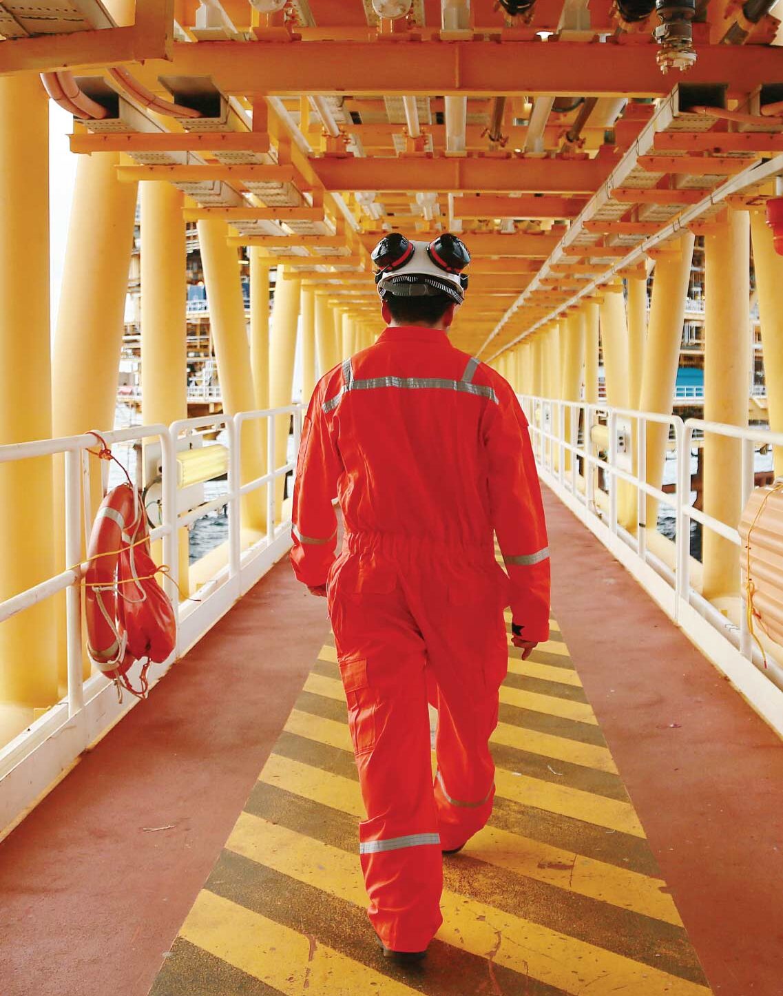 Person in safety coveralls and helmet walking along a marked industrial walkway.