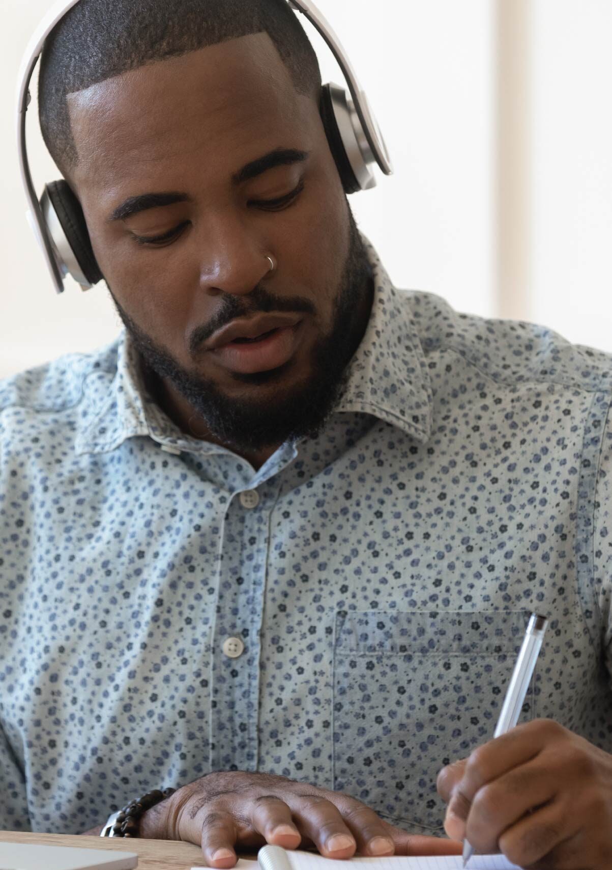 Person wearing headphones writing notes with a pen at a desk.