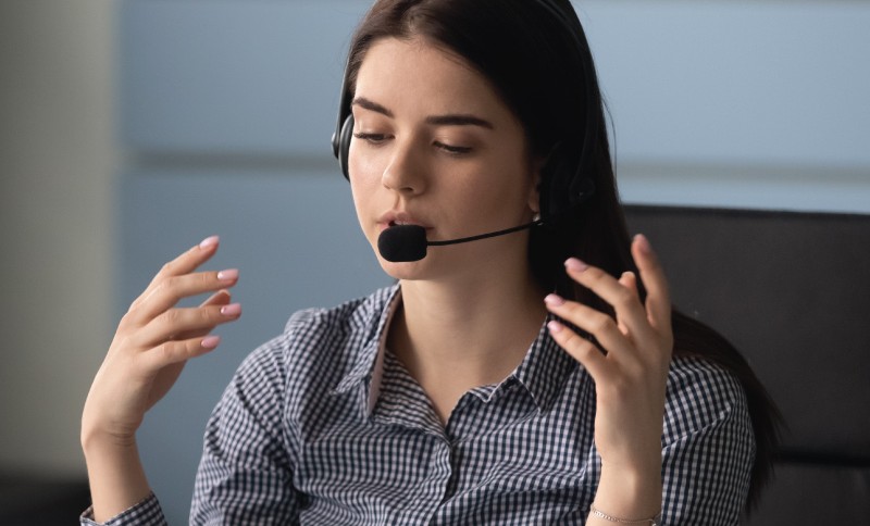 Person wearing a headset speaking and gesturing during an online support call at a desk.