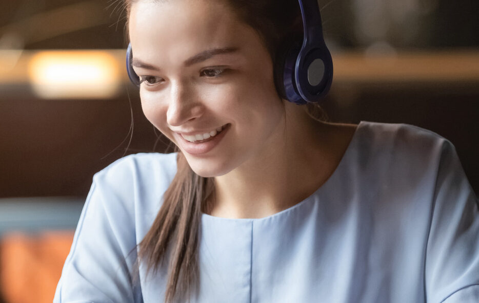 Person wearing headphones uses a laptop while seated indoors at a desk.