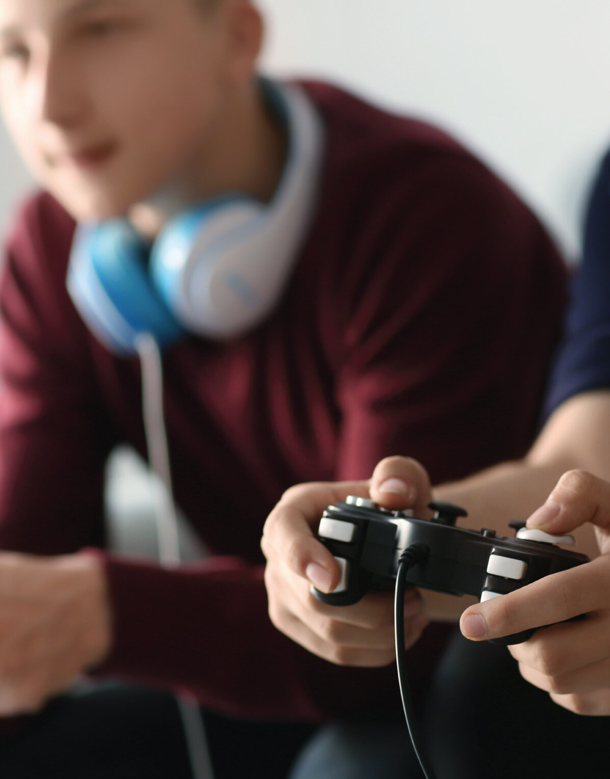 Close-up of hands holding a game controller while others sit nearby wearing headphones.