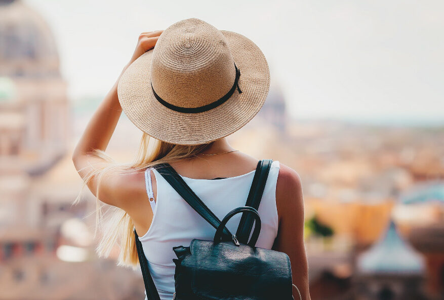 Person wearing a hat and backpack looks over a cityscape with historic buildings in the background.