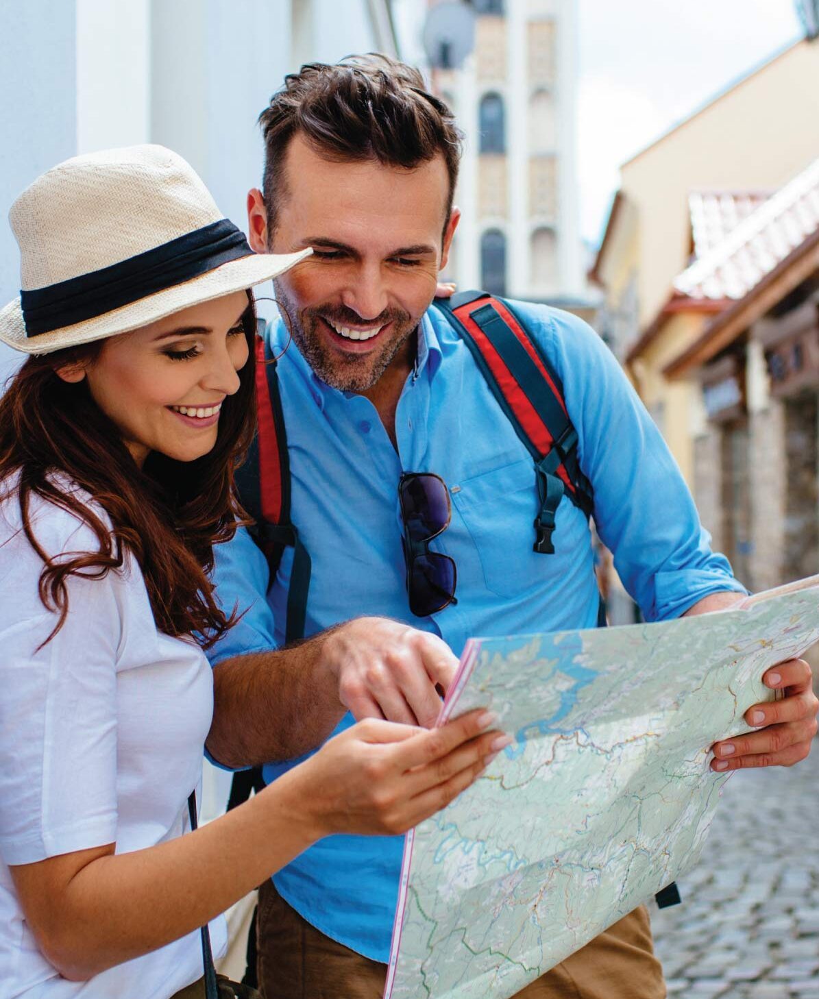 Two people use a paper map together while standing on a cobbled street in a city centre.