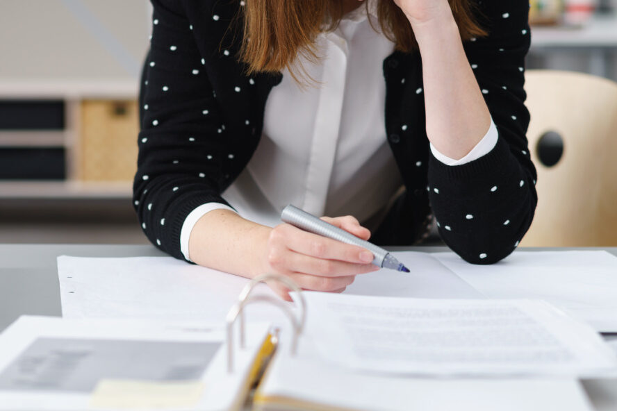 Close-up of a person holding a pen and writing on documents at a desk.