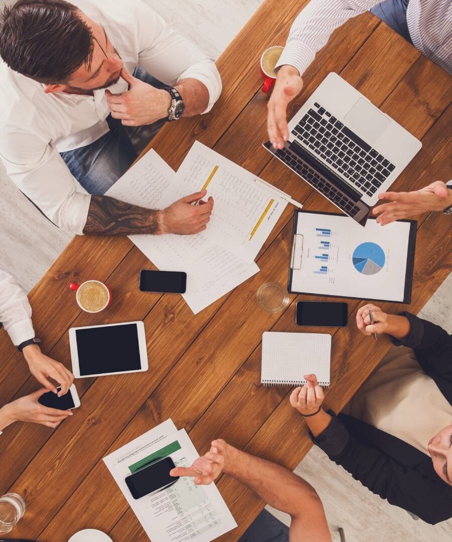 Overhead view of several people reviewing reports, charts and devices around a table.