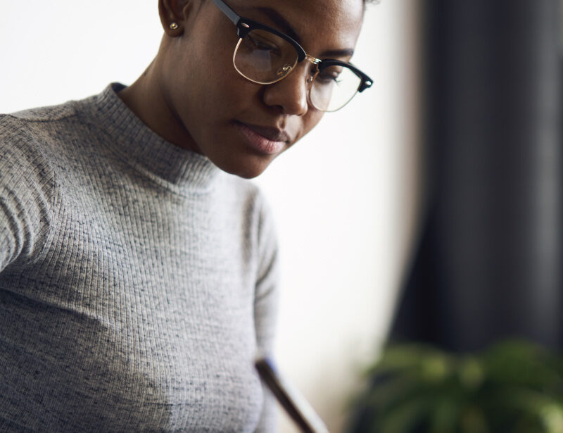 Close-up of a person wearing glasses writing on paper at a desk with a phone nearby.