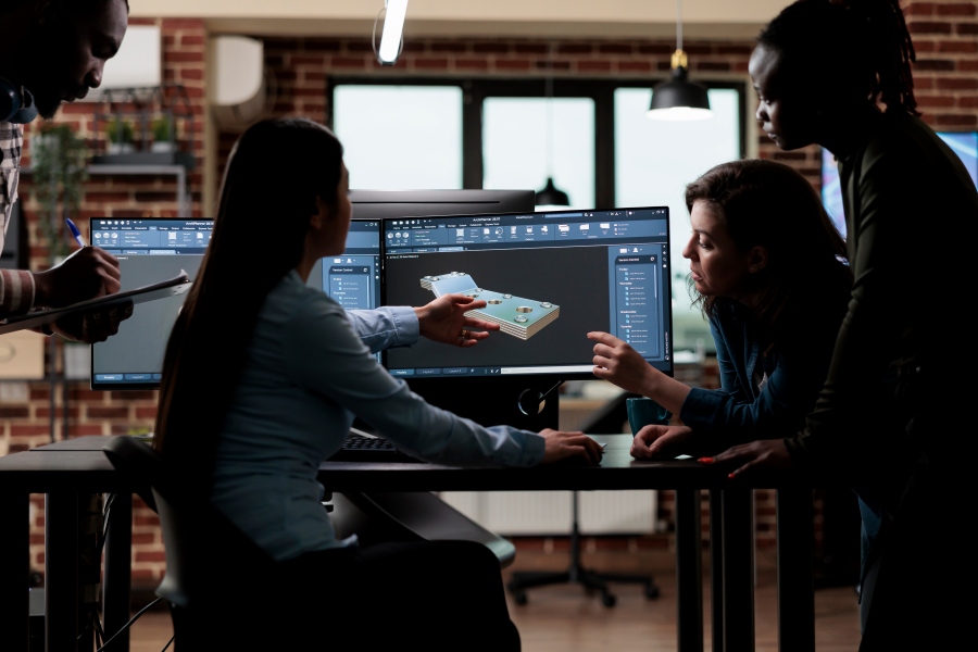 Group gathered around computer screens reviewing a 3D model and pointing at details.