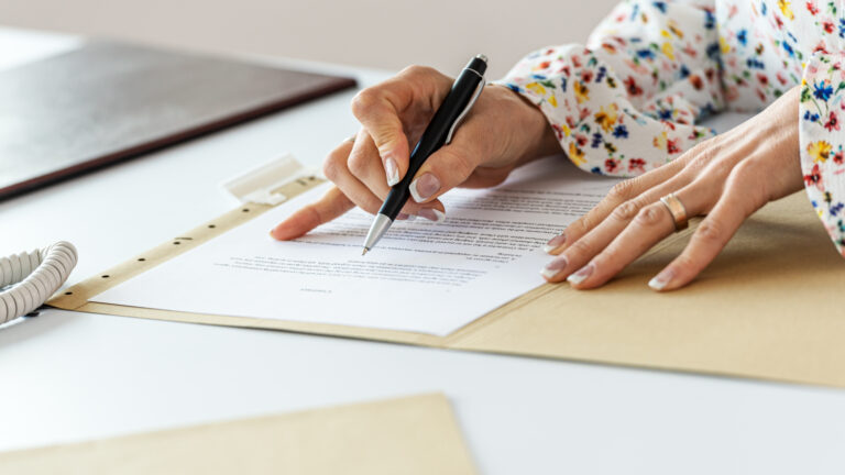 Close-up of a hand holding a pen and signing a printed document on a desk.