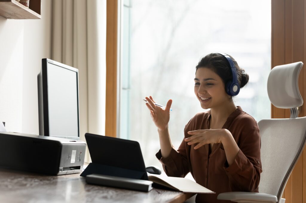 Person wearing headphones gestures while speaking during a video call at a desk.